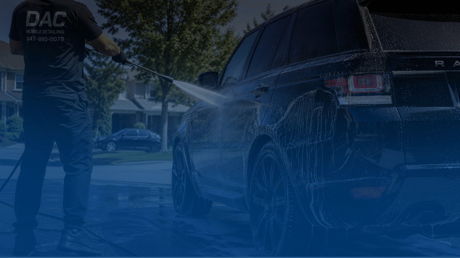 Person pressure washing a dark SUV in a residential driveway on a sunny day